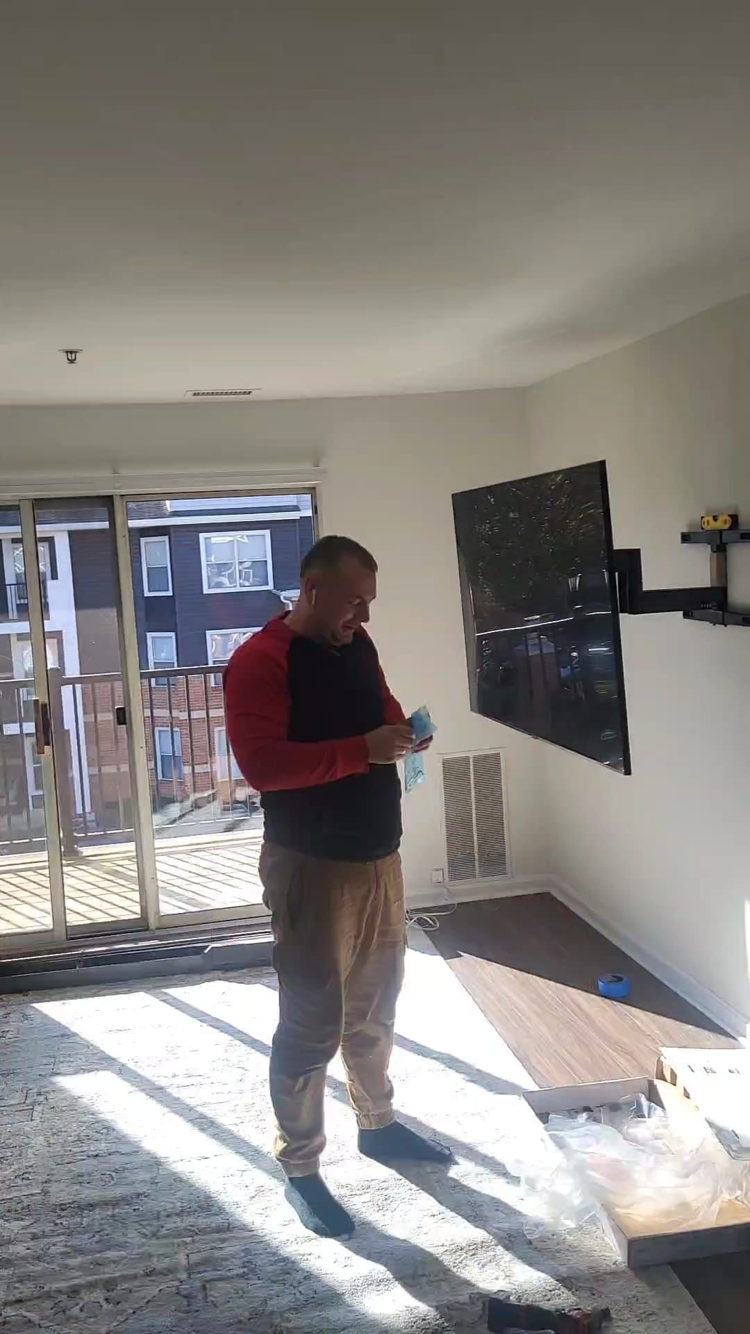 Person standing in a bright living room with a mounted TV and an open box on the floor.