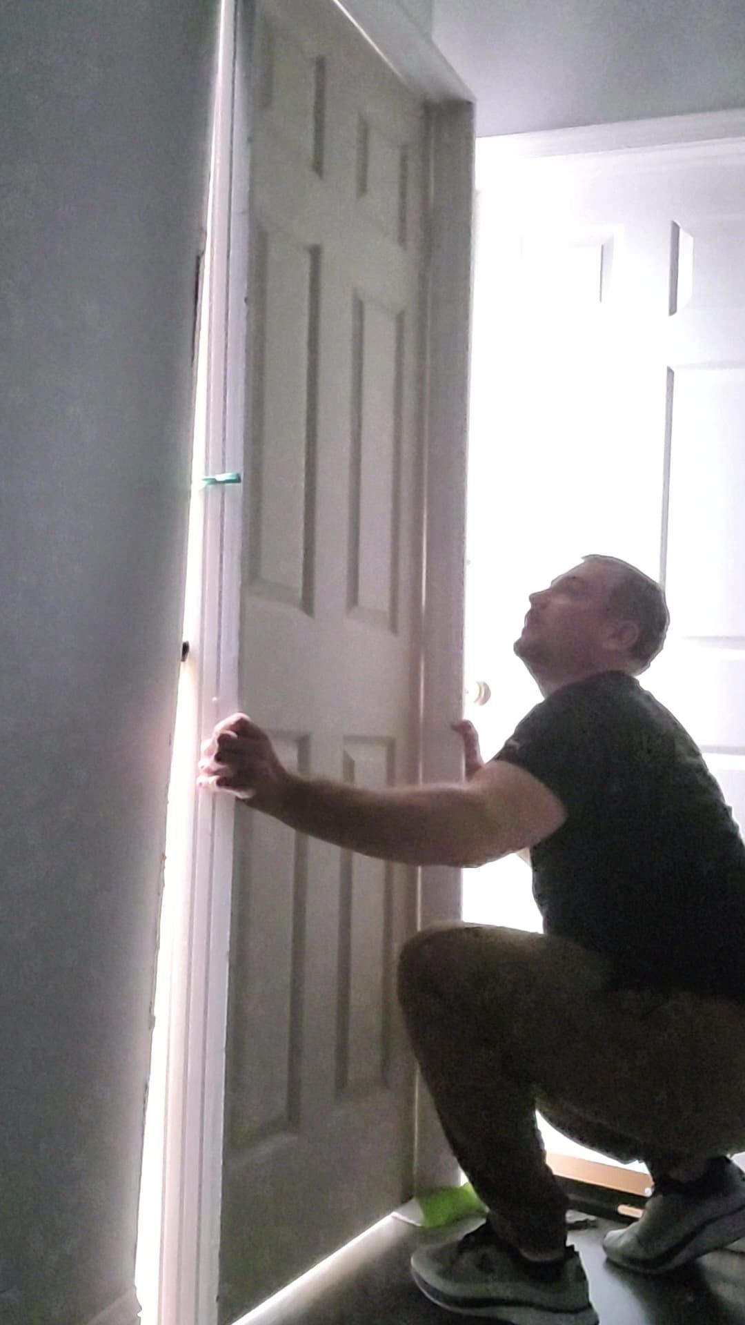 Person squatting down while opening a door slightly, with light streaming in from behind the door.